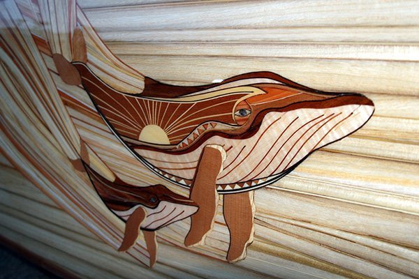 close up of wood design and mother of pearl detail on a michael rumsey decorative surfboard with whales titled ohana