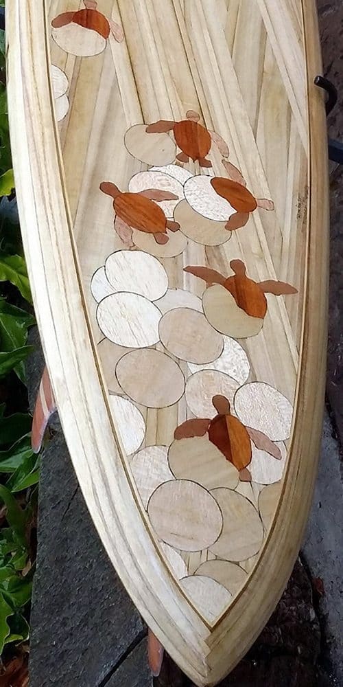 A beautiful wood inlay surfboard with the pattern being many turtles swimming