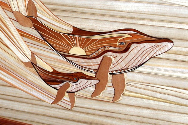 A beautiful wood inlay surfboard with the pattern of a family of whales